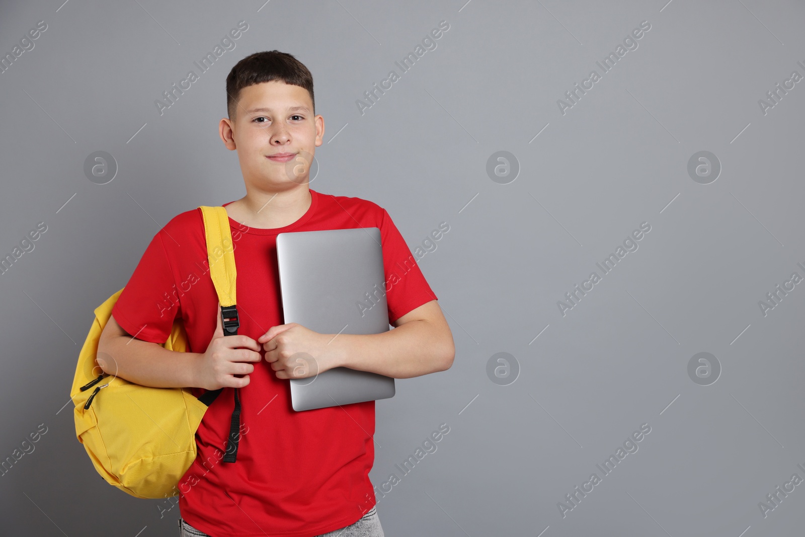 Teenage boy with laptop and backpack on grey background, space for text Photo of Teenage boy with laptop and backpack on grey background, space for text