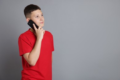 Photo of Teenage boy talking on smartphone against grey background, space for text