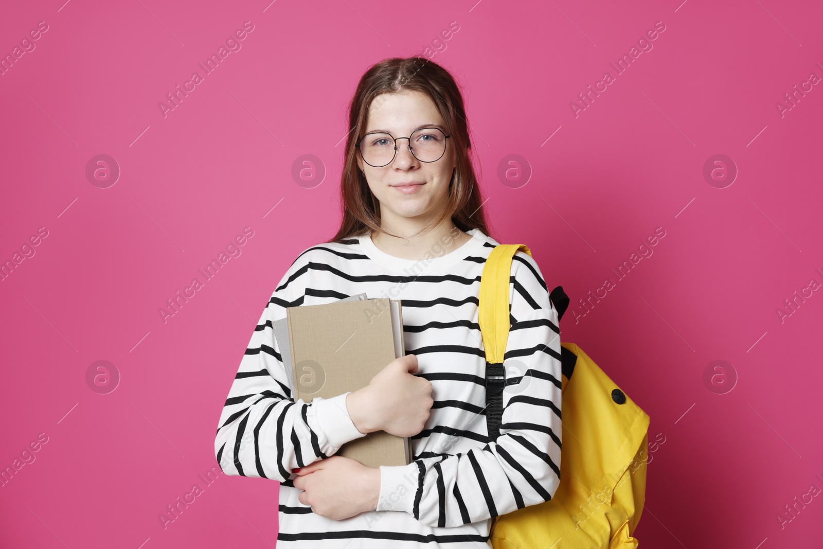 Teenage girl in glasses with backpack and books on crimson background Photo of Teenage girl in glasses with backpack and books on crimson background