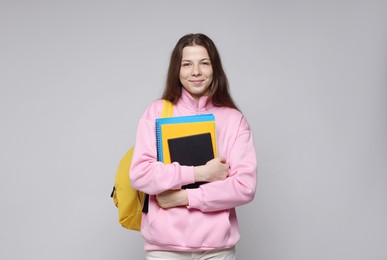 Photo of Teenage girl with backpack and notebooks on light grey background
