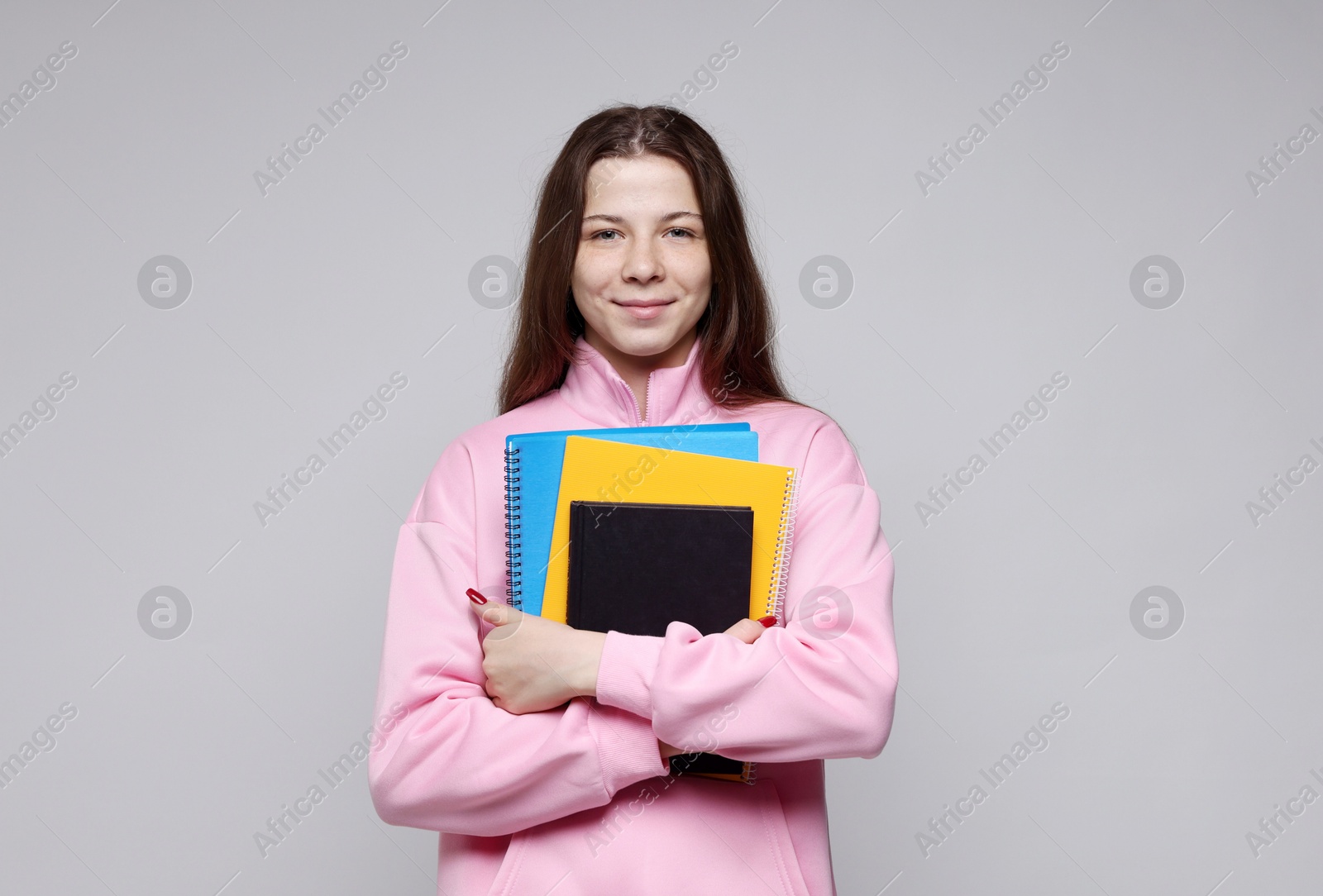 Teenage girl with notebooks on light grey background Photo of Teenage girl with notebooks on light grey background