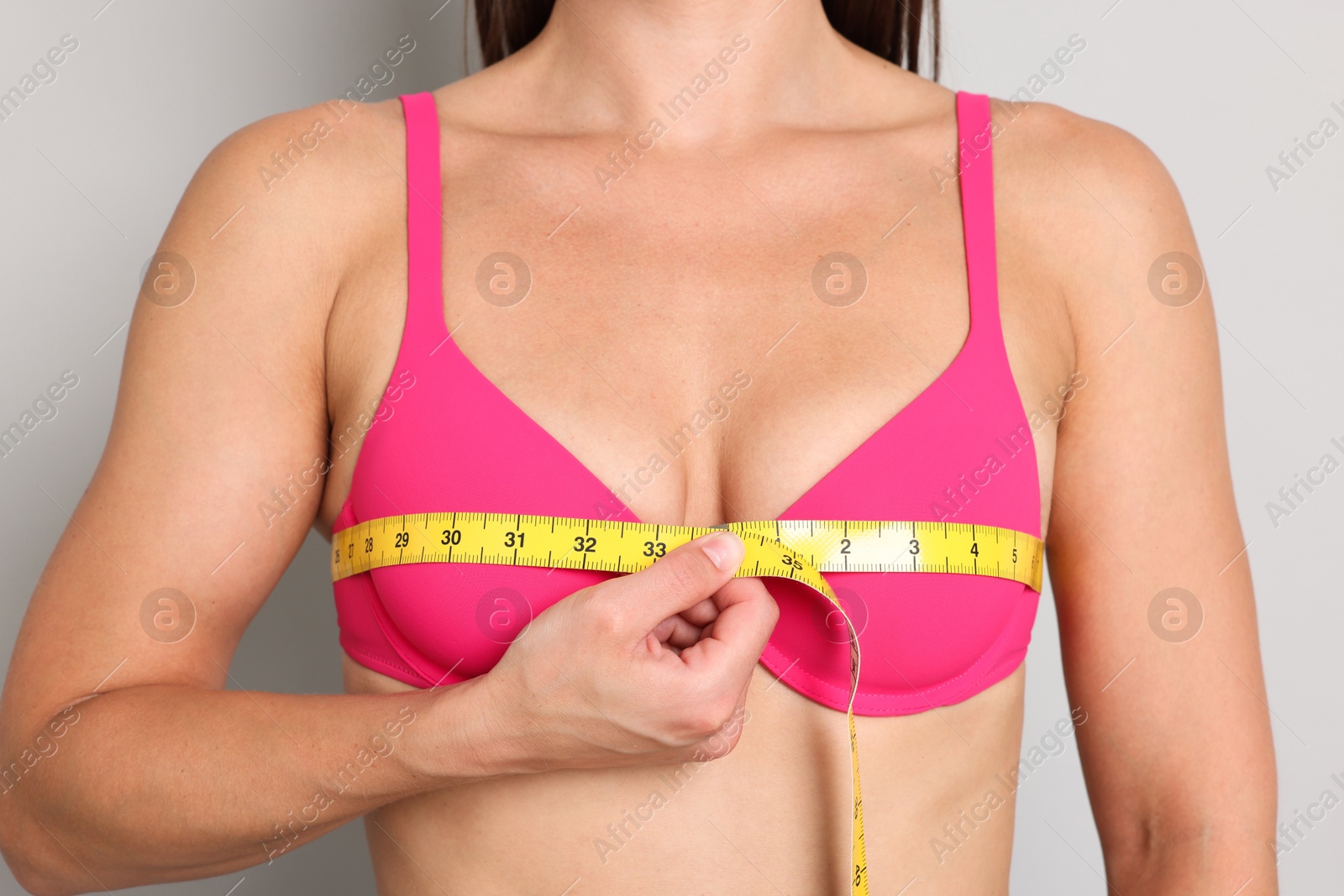 Photo of Woman in beautiful bra measuring breast circumference on light grey background, closeup