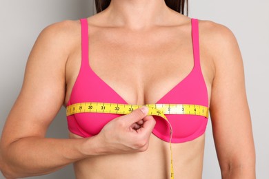 Photo of Woman in beautiful bra measuring breast circumference on light grey background, closeup