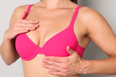 Photo of Woman wearing beautiful pink bra on light grey background, closeup