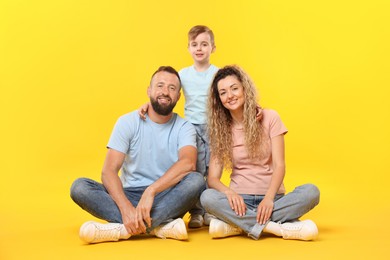 Photo of Happy family. Parents and their son posing on yellow background