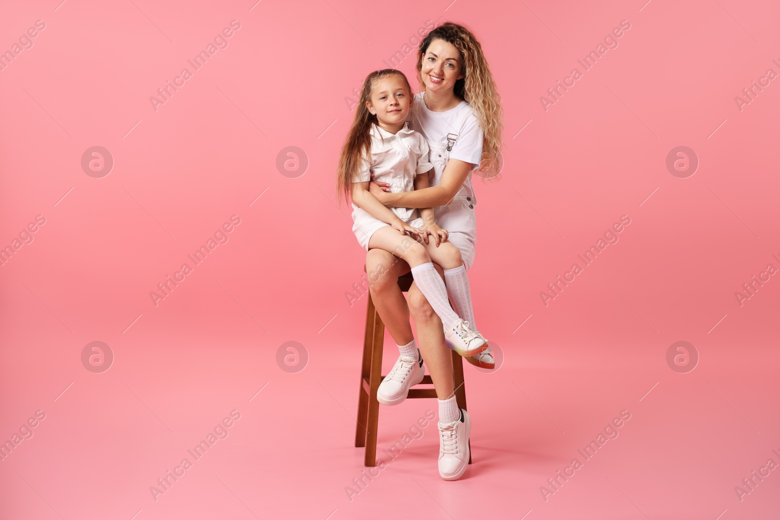 Photo of Family. Happy mother and her daughter posing on stool against pink background