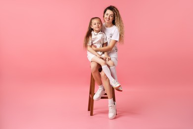 Photo of Family. Happy mother and her daughter posing on stool against pink background