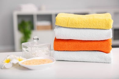 Photo of Stack of colorful towels, sea salt, swabs and plumeria flowers on white table indoors