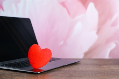 Photo of Online dating site. Decorative heart and laptop on wooden table, closeup. Space for text