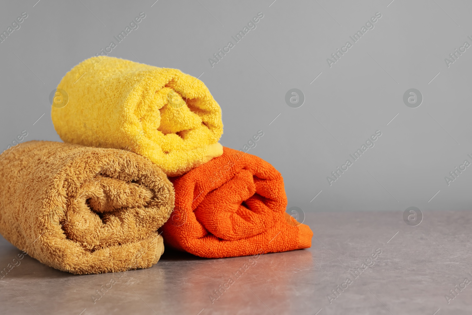 Photo of Rolled colorful towels on grey table, closeup. Space for text