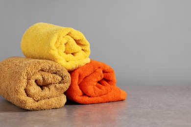 Photo of Rolled colorful towels on grey table, closeup. Space for text