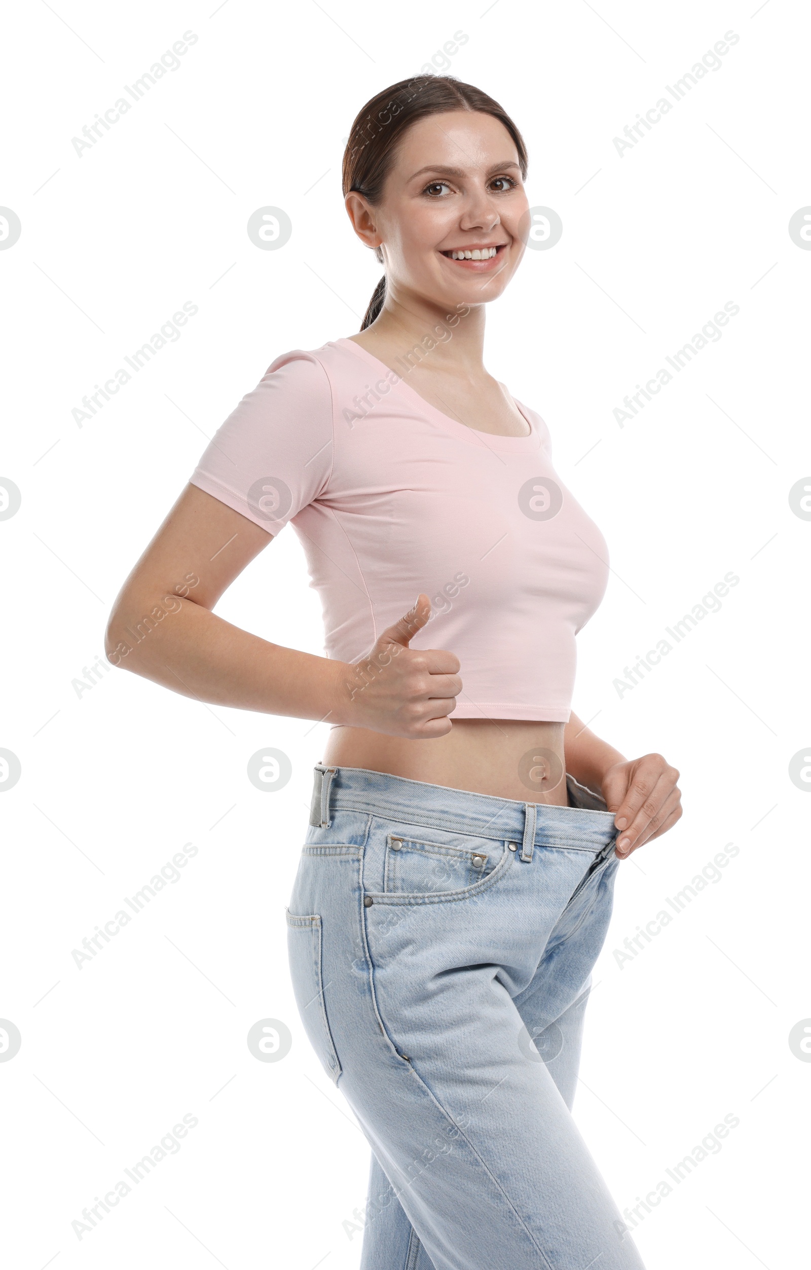 Photo of Beautiful woman wearing old jeans after weight loss and showing thumbs up on white background