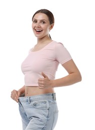 Photo of Beautiful woman wearing old jeans after weight loss and showing thumbs up on white background
