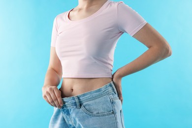 Photo of Woman wearing old jeans after weight loss on light blue background, closeup