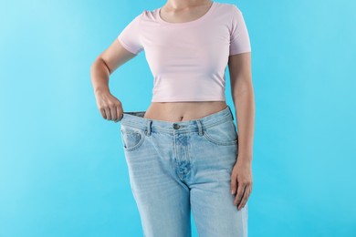 Photo of Woman wearing old jeans after weight loss on light blue background, closeup