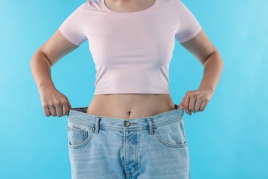Photo of Woman wearing old jeans after weight loss on light blue background, closeup