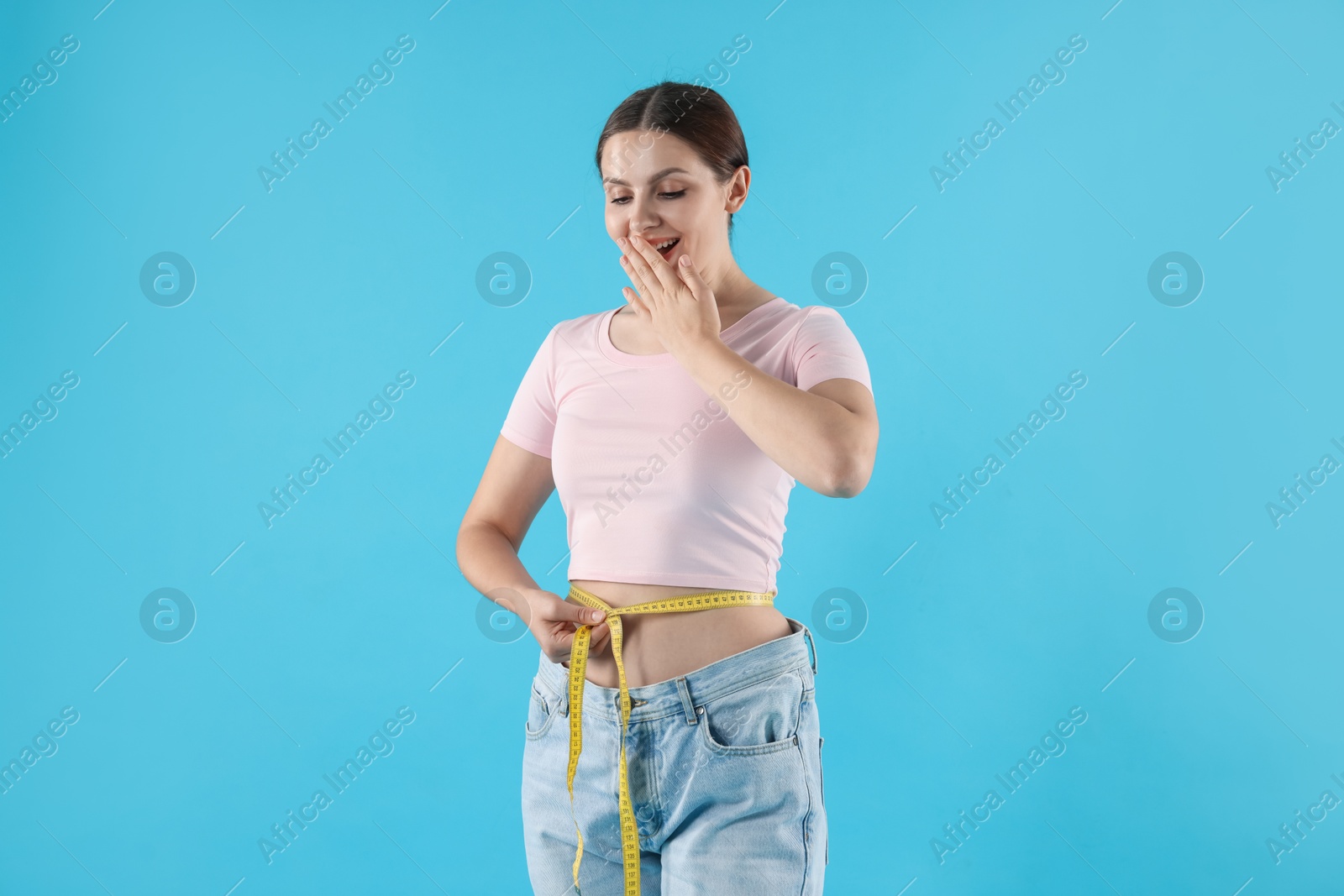 Photo of Beautiful woman with measuring tape wearing old jeans after weight loss on light blue background