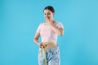 Photo of Beautiful woman with measuring tape wearing old jeans after weight loss on light blue background
