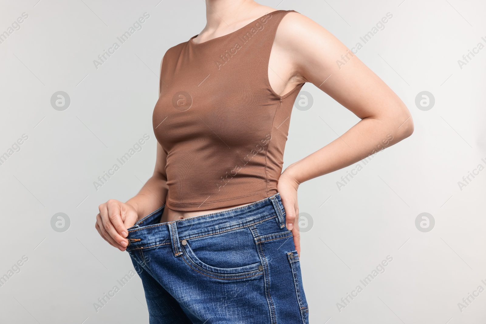 Woman wearing old jeans after weight loss on light grey background, closeup Photo of Woman wearing old jeans after weight loss on light grey background, closeup
