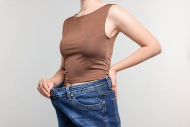 Photo of Woman wearing old jeans after weight loss on light grey background, closeup