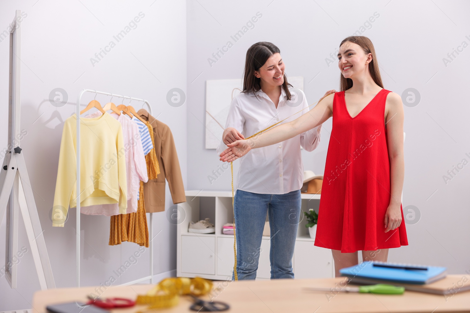 Photo of Tailor measuring woman's arm with tape in atelier