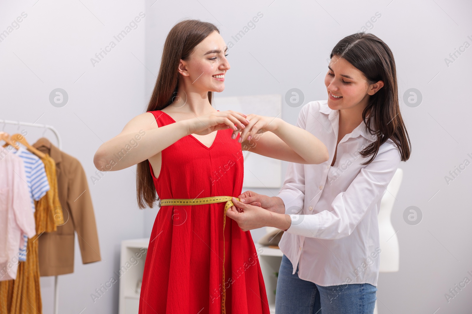 Photo of Tailor measuring woman's waist with tape in atelier