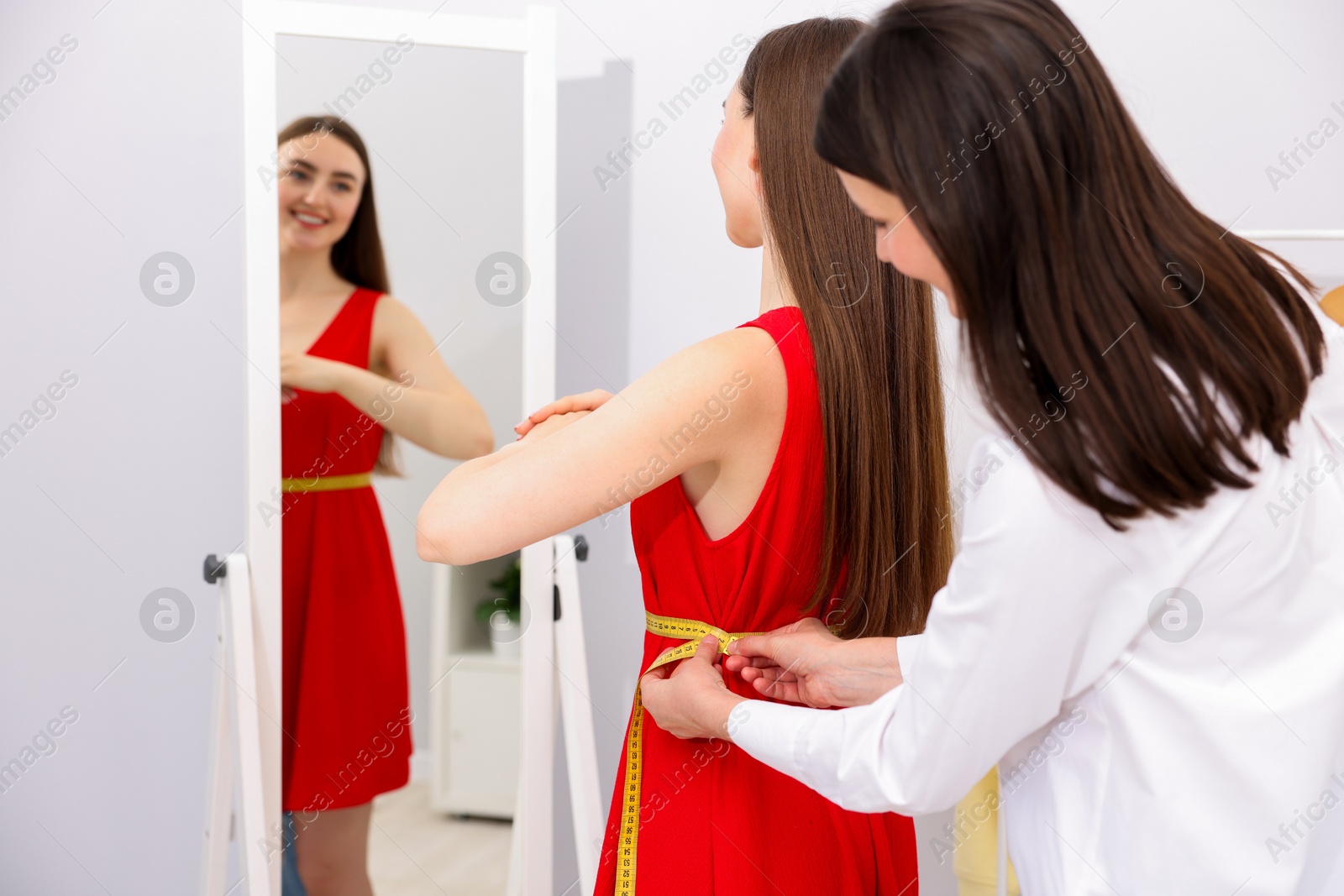 Photo of Tailor measuring woman's waist with tape in atelier