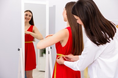 Photo of Tailor measuring woman's waist with tape in atelier