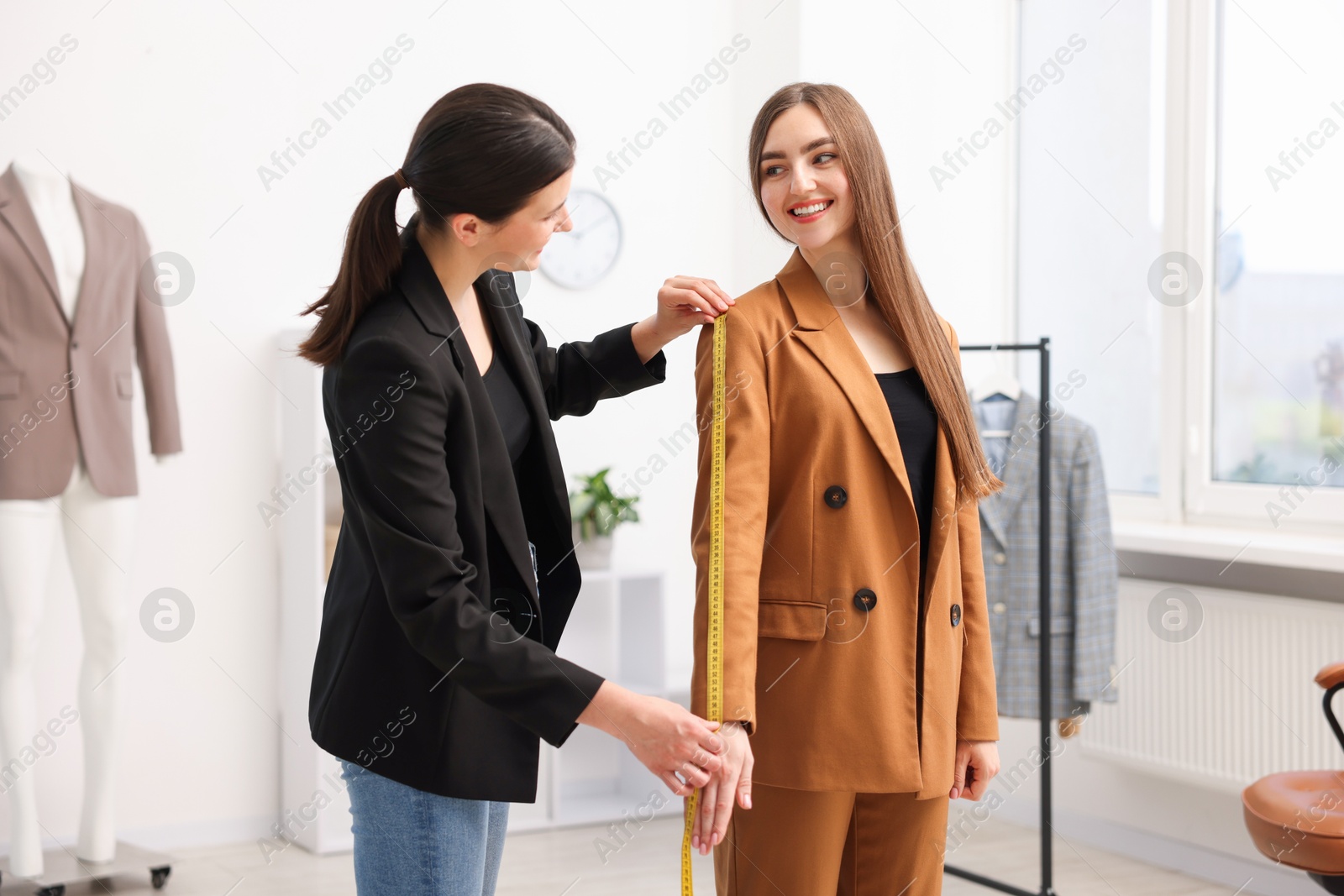 Photo of Tailor measuring jacket sleeve on woman in atelier