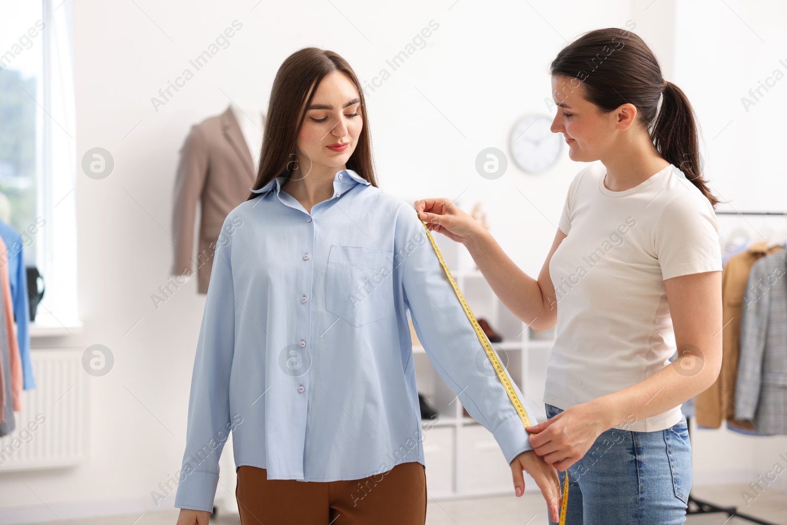 Photo of Tailor measuring woman's arm with tape in atelier