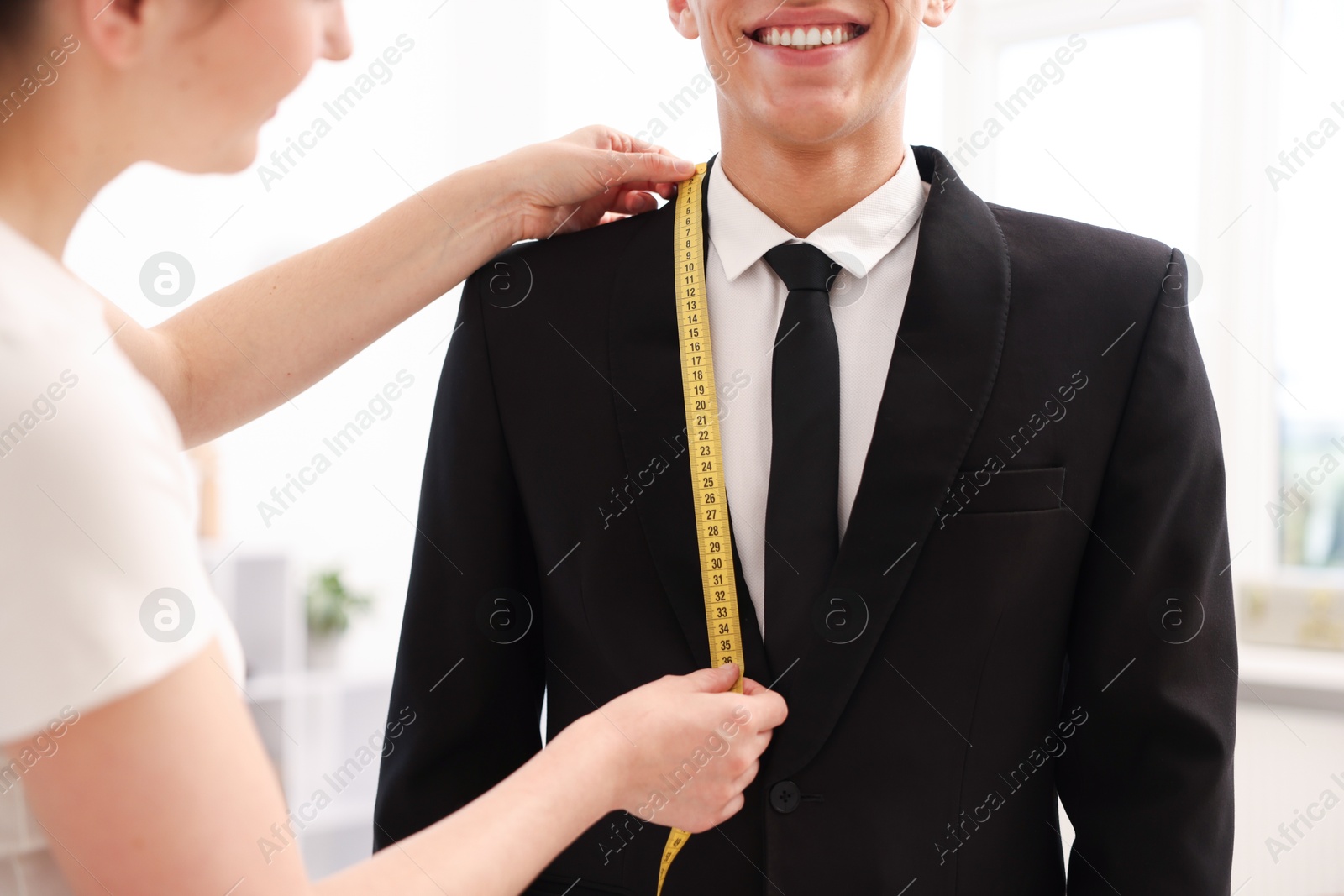 Photo of Tailor measuring jacket on man in atelier, closeup