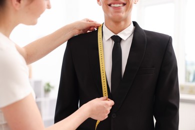 Photo of Tailor measuring jacket on man in atelier, closeup