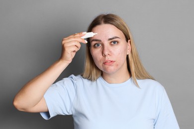Photo of Woman applying cream onto face on grey background. Acne treatment