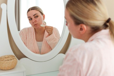 Photo of Woman applying cream onto face near mirror indoors. Acne treatment