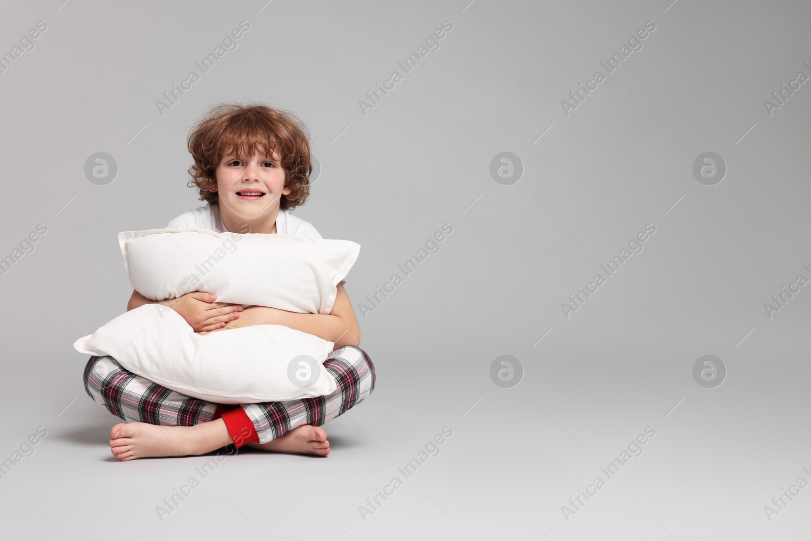 Photo of Cute little boy in pajamas with pillow on grey background. Space for text