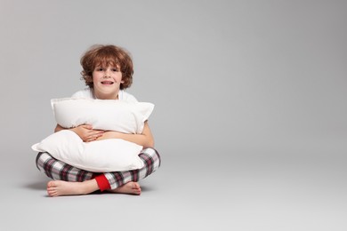 Photo of Cute little boy in pajamas with pillow on grey background. Space for text