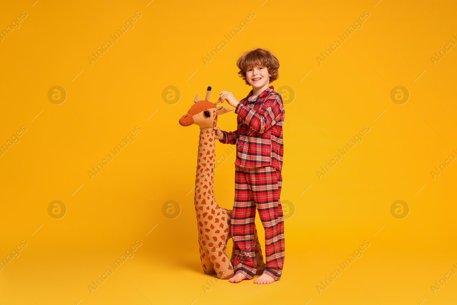 Photo of Cute little boy in pajamas with toy giraffe on yellow background