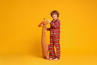 Photo of Cute little boy in pajamas with toy giraffe on yellow background