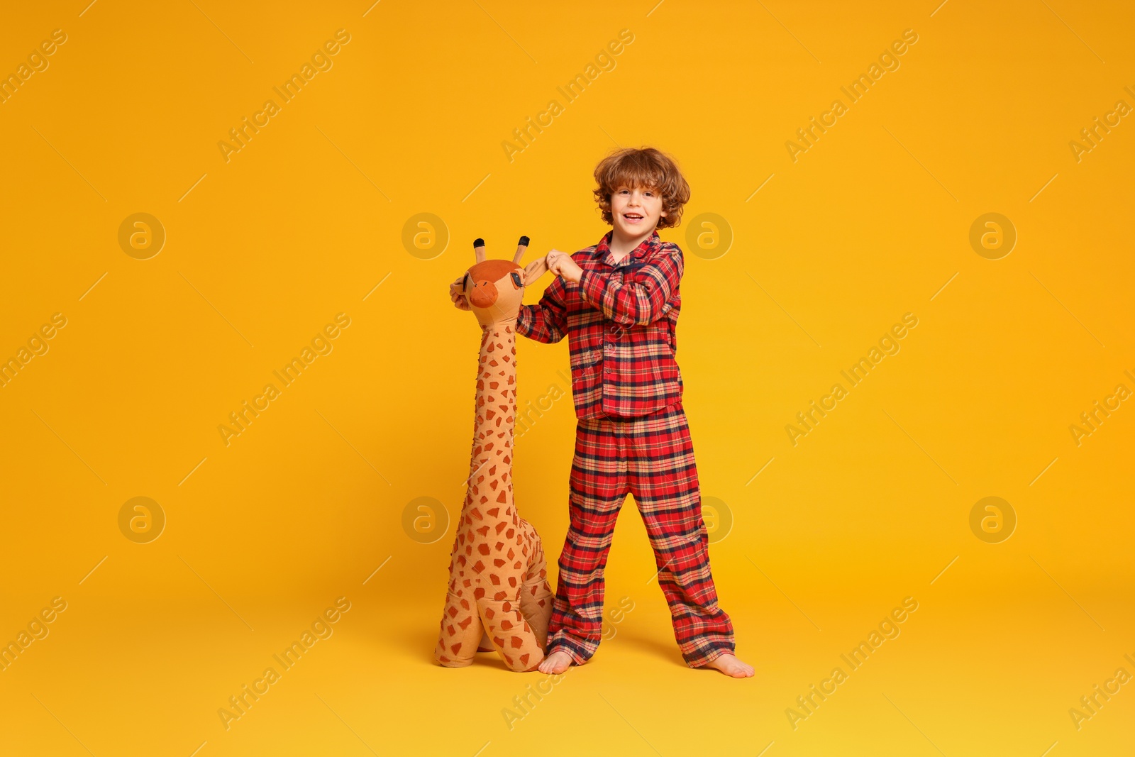 Photo of Cute little boy in pajamas with toy giraffe on yellow background