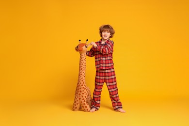 Photo of Cute little boy in pajamas with toy giraffe on yellow background
