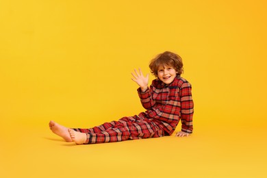 Photo of Cute little boy in pajamas waving on yellow background. Space for text