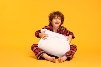 Photo of Cute little boy in pajamas with pillow on yellow background