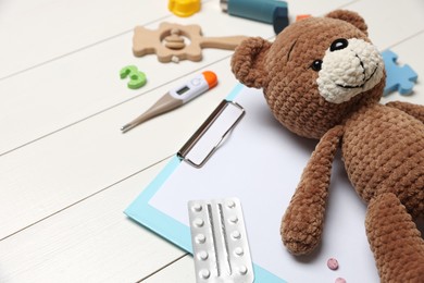 Photo of Pediatrics concept. Toy bear, clipboard and pills on white wooden background, closeup
