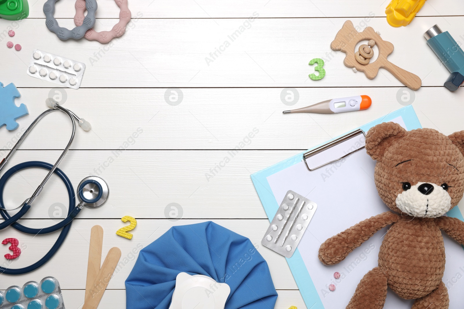 Photo of Pediatrics concept. Toy bear, clipboard and pills on white wooden background, flat lay. Space for text