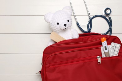 Photo of Pediatrics concept. Toy bear with stethoscope and first aid kit on white wooden background, top view