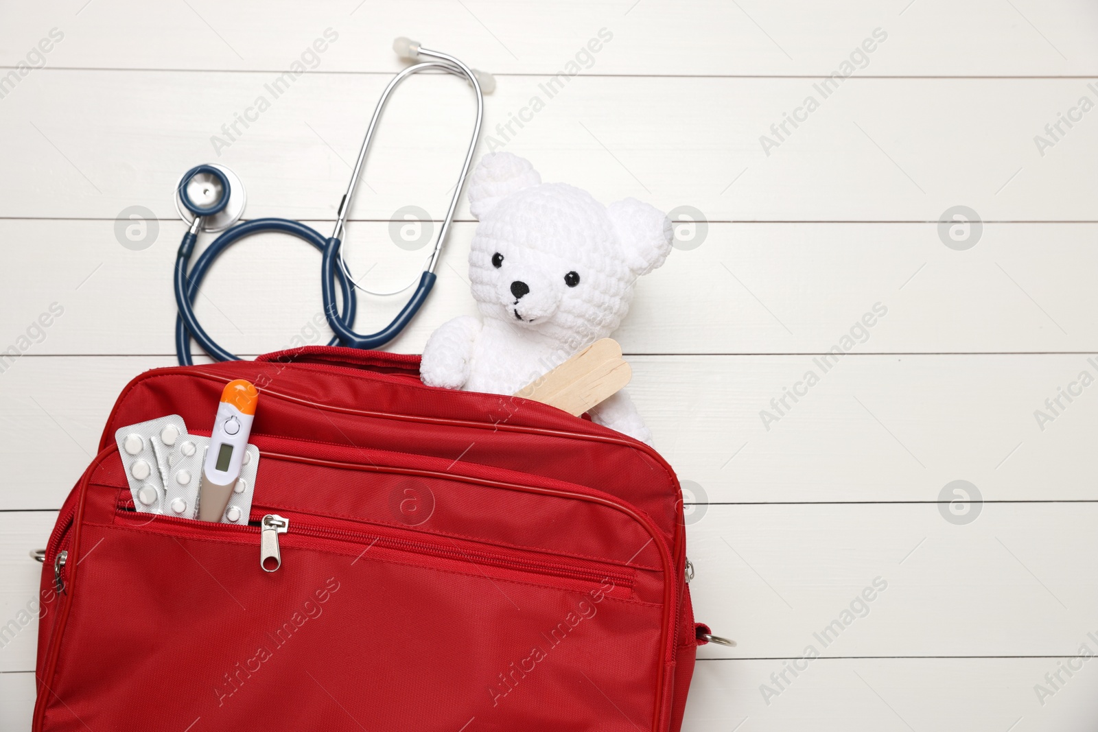 Photo of Pediatrics concept. Toy bear with stethoscope and first aid kit on white wooden background, top view