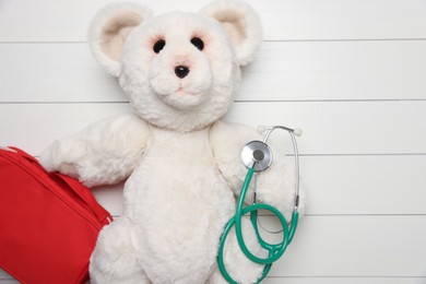 Photo of Pediatrics concept. Toy bear with stethoscope and first aid kit on white wooden background, top view