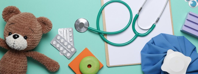 Photo of Pediatrics concept. Toy bear with stethoscope and pills on turquoise background, flat lay