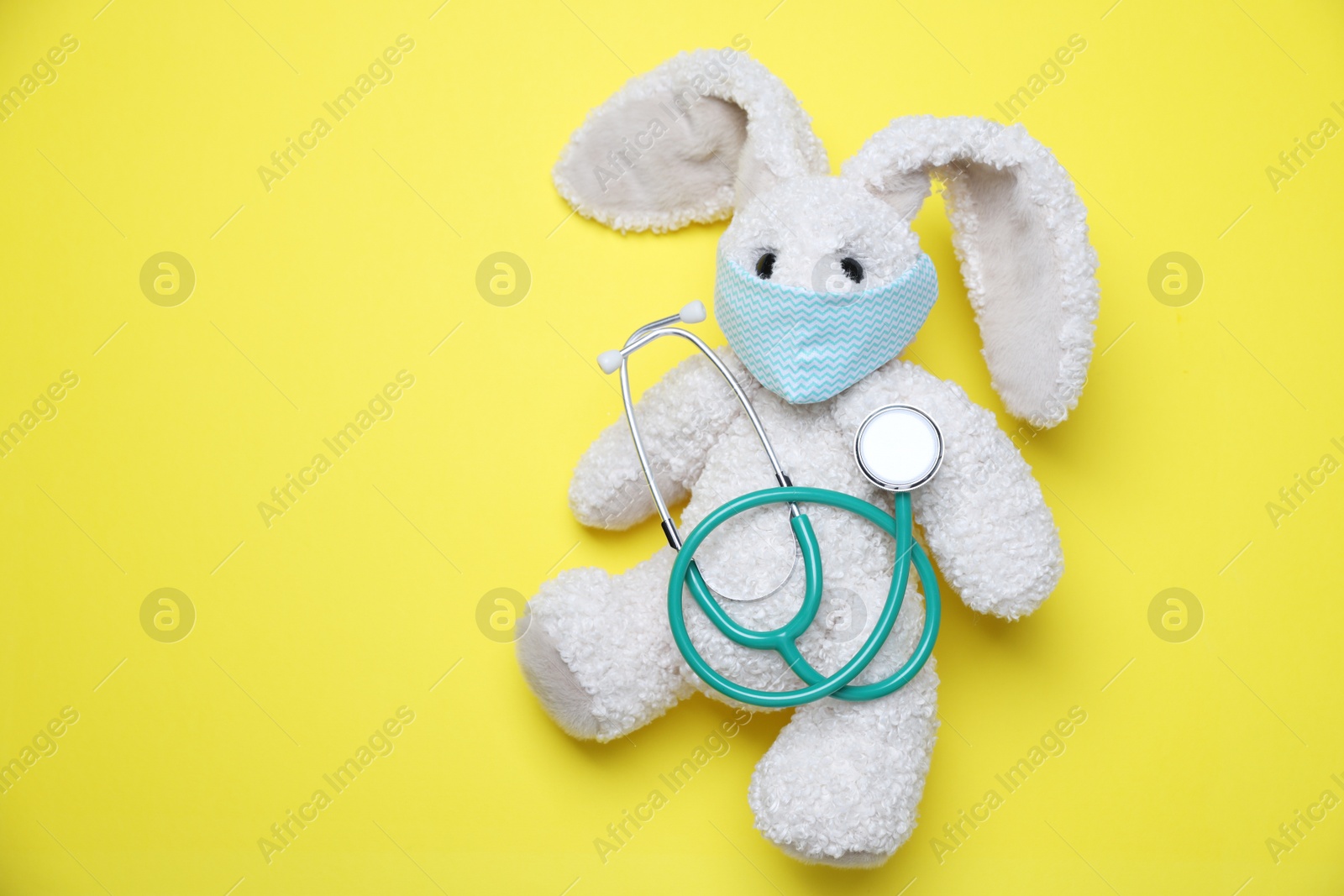 Photo of Pediatrics concept. Toy bunny with stethoscope on yellow background, top view. Space for text