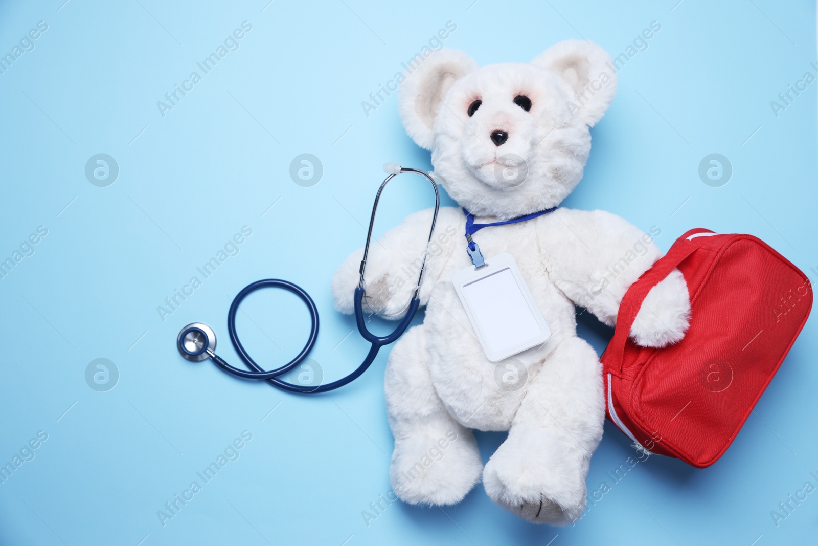 Photo of Pediatrics concept. Toy bear with stethoscope and first aid kit on light blue background, top view. Space for text